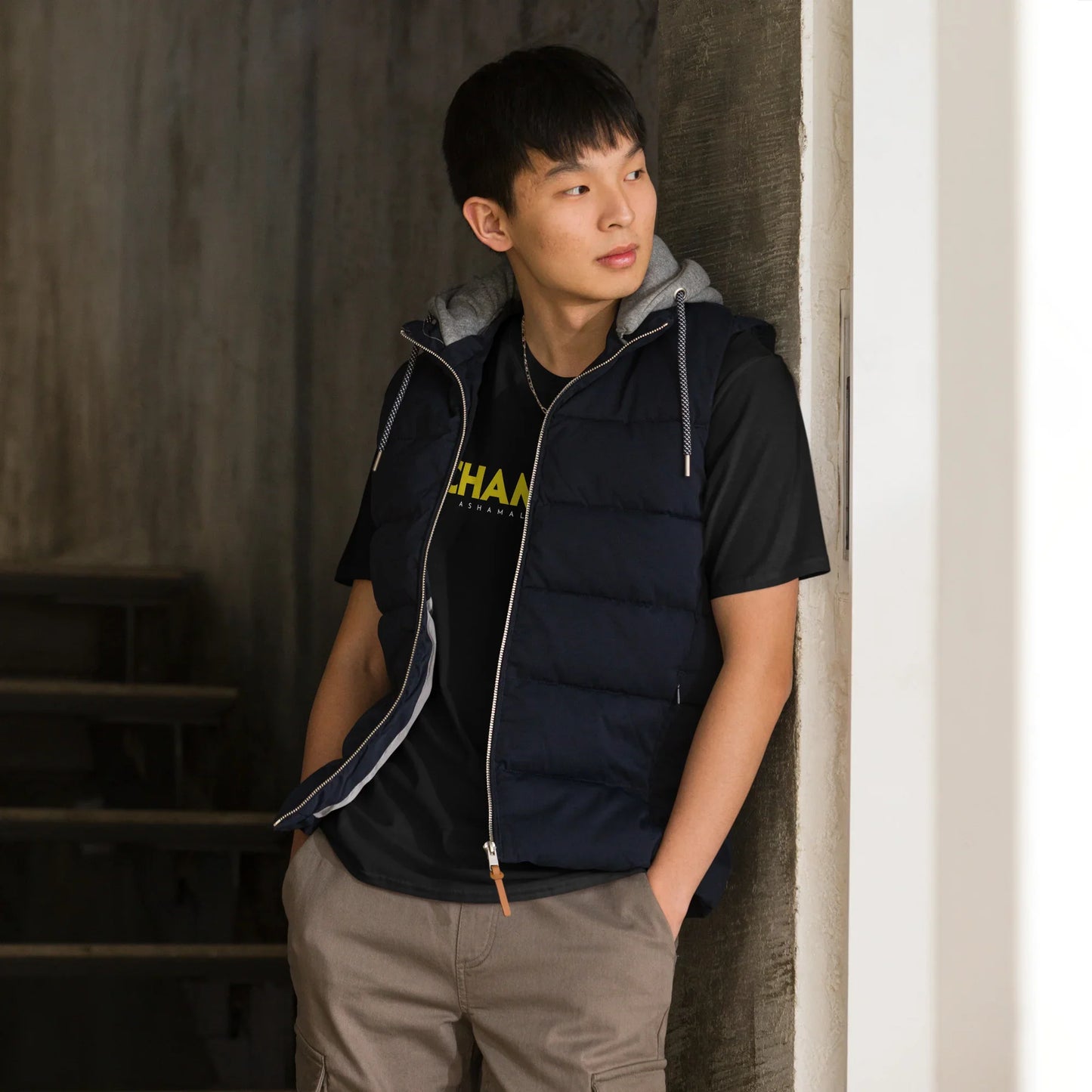 Man wearing a black short sleeve t-shirt with yellow text 'Champion' and white text 'AShamaluevMusic' and a blue sleeveless jacket with a zipper in front of a staircase.