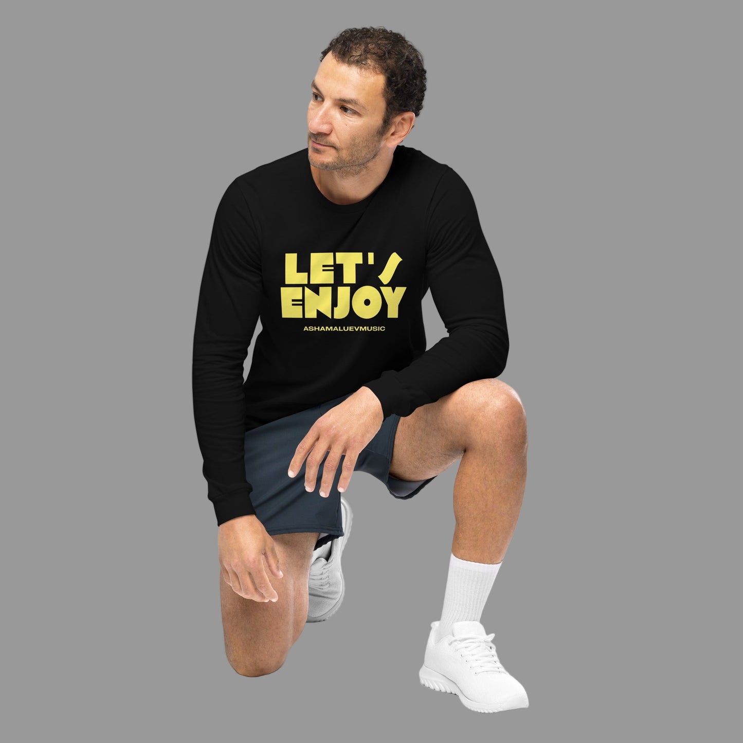 Man wearing a black long-sleeve shirt with yellow text and gray shorts on a grey background