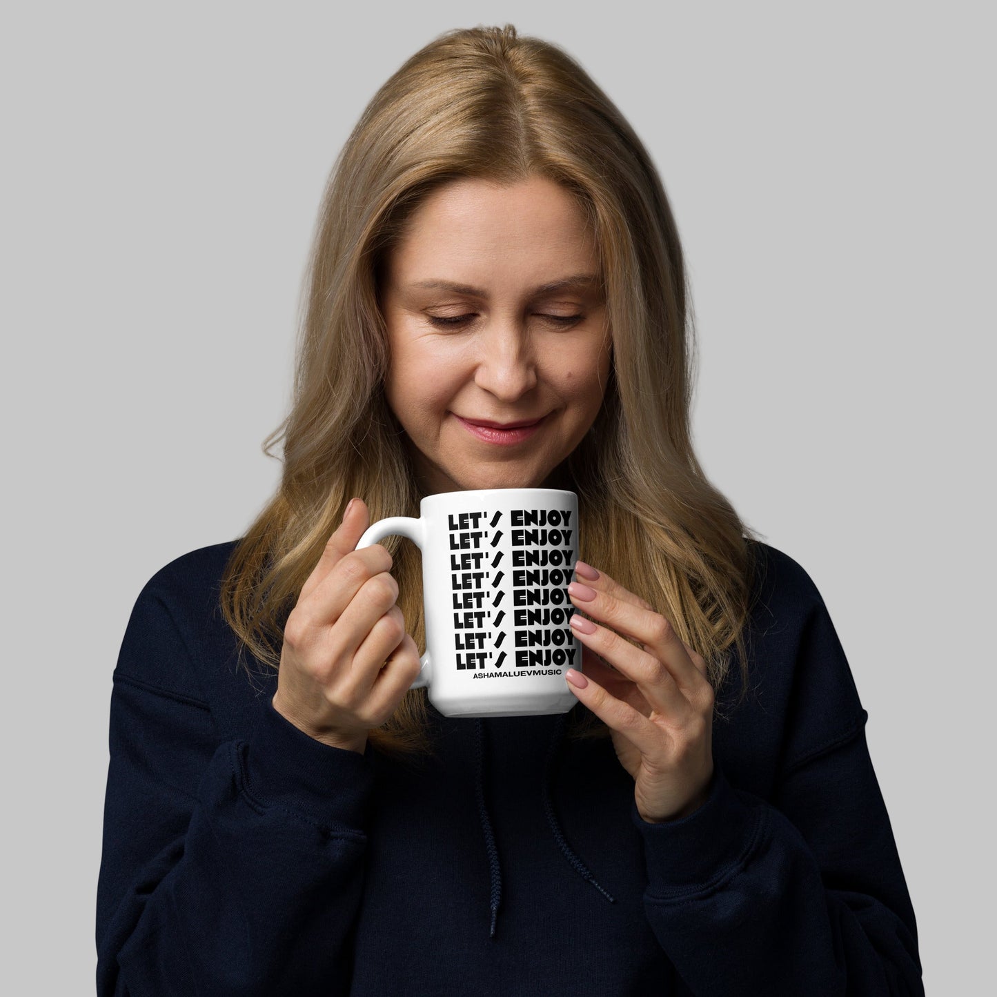 Woman holding a white mug with text 'Let's Enjoy' on a grey background