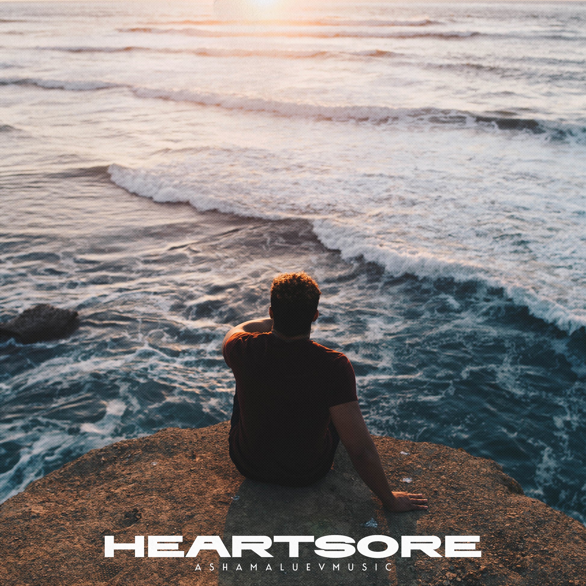 Cover art of the music track 'Heartsore' by AShamaluevMusic, which shows the person sitting on a rock by the ocean.