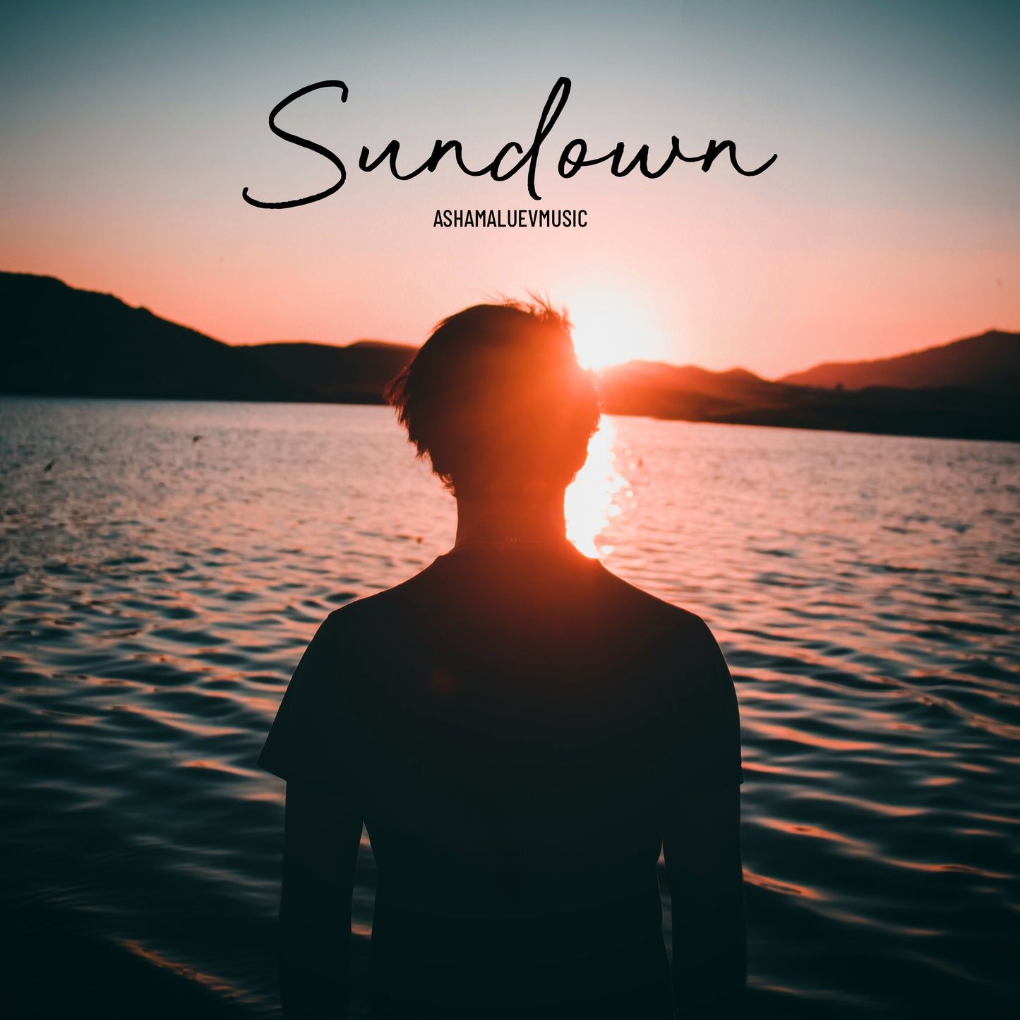 Cover art of the music track 'Sundown' by AShamaluevMusic, which shows the person standing by a lake with sunset.