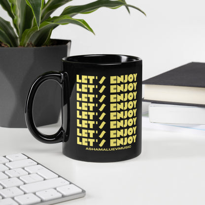 Black mug with yellow text 'LET'S ENJOY' on a desk with a plant and books in the background