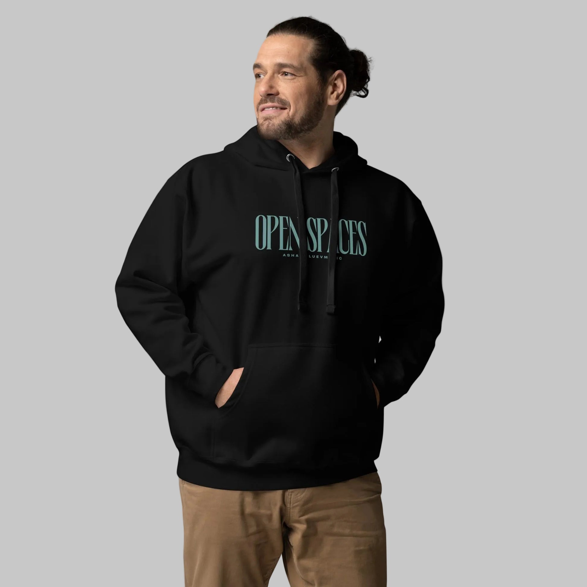 Man wearing a black premium hoodie with turquoise text 'Open Spaces' and 'AShamaluevMusic' on a gray background.