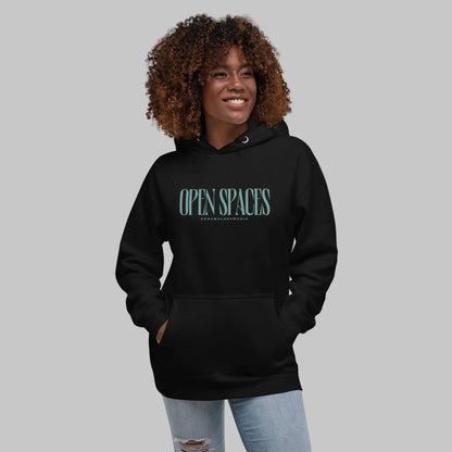 Woman wearing a black premium hoodie with turquoise text 'Open Spaces' and 'AShamaluevMusic' on a gray background.