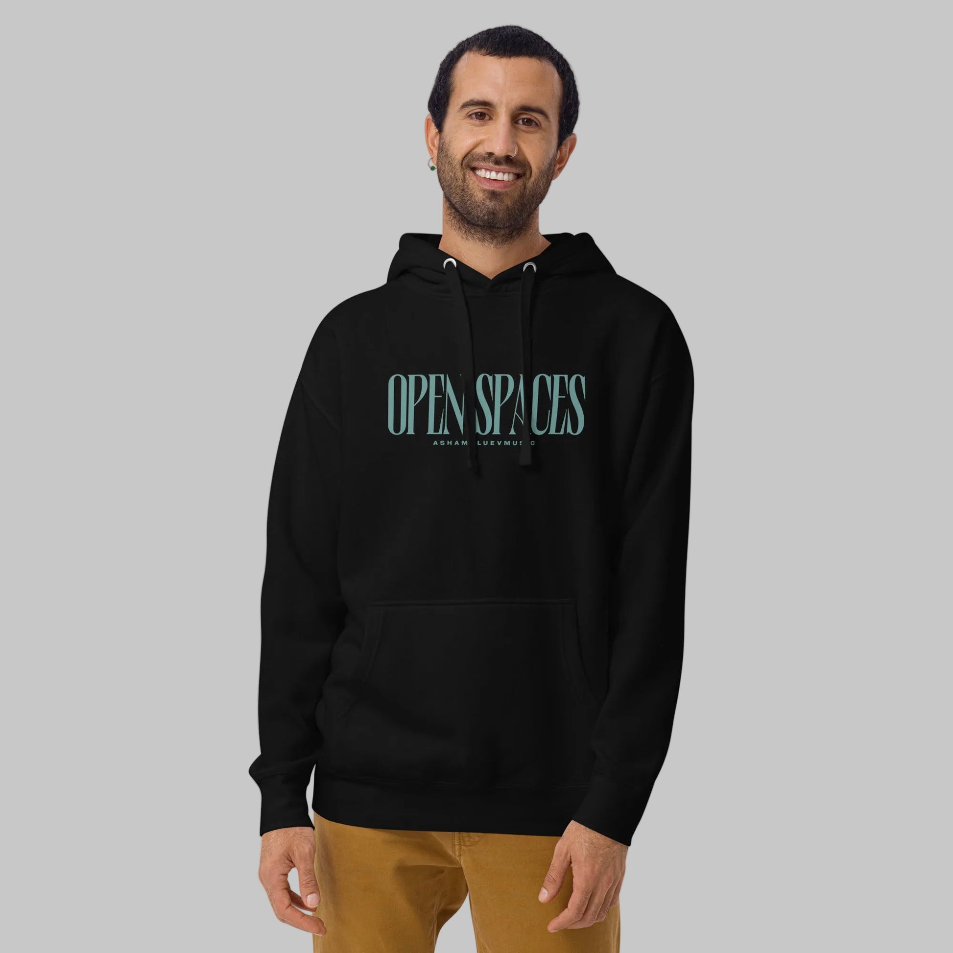 Man wearing a black premium hoodie with text 'Open Spaces' and 'AShamaluevMusic' on a gray background.