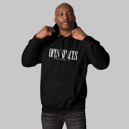 Man wearing a black unisex pullover hoodie with white text 'Open Spaces' and 'AShamaluevMusic' on a gray background.