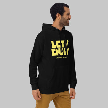 Man wearing a black unisex pullover hoodie with yellow text 'Let's Enjoy' and 'AShamaluevMusic' on a gray background.