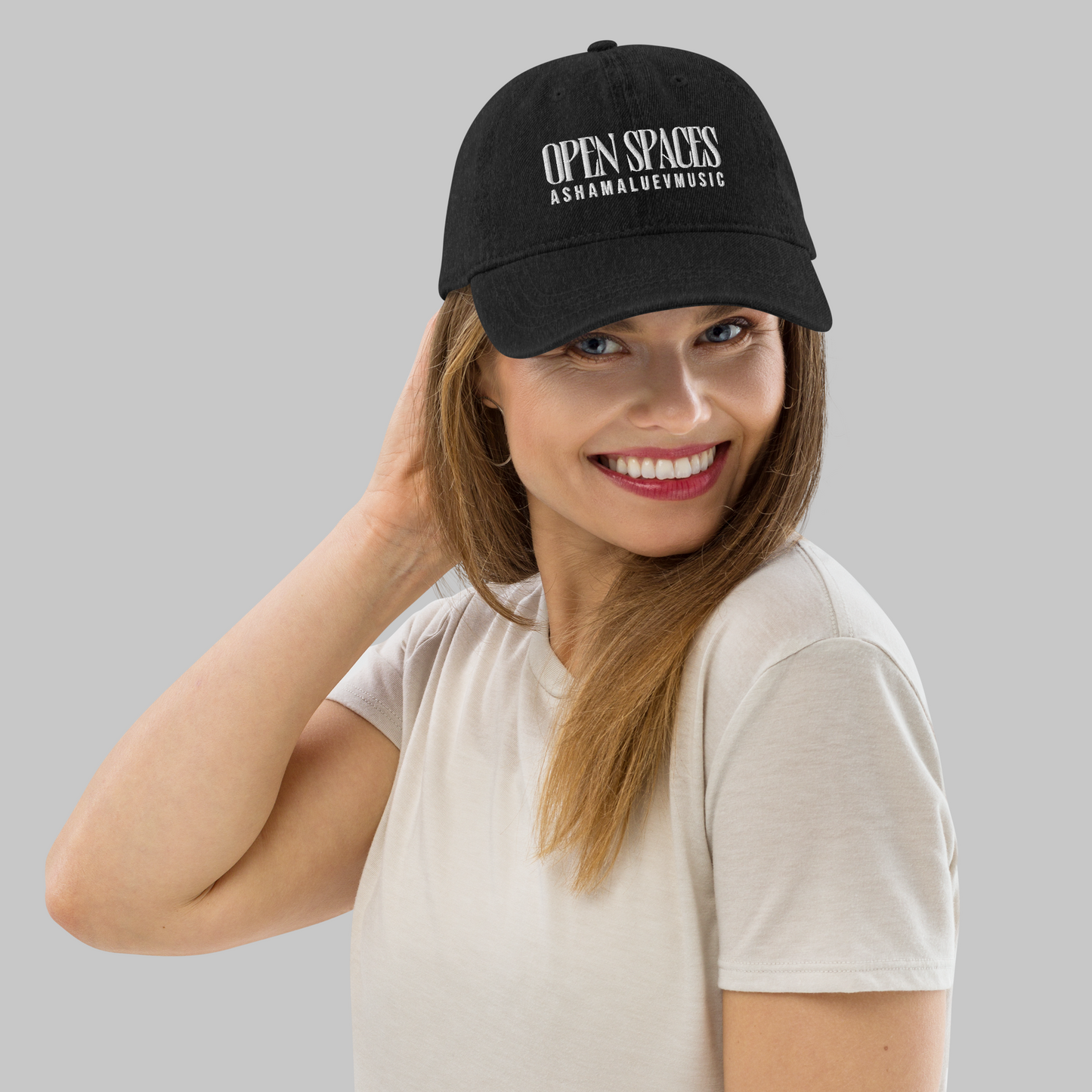 Woman wearing a black denim cap with text 'Open Spaces' and 'AShamaluevMusic' on a gray background.