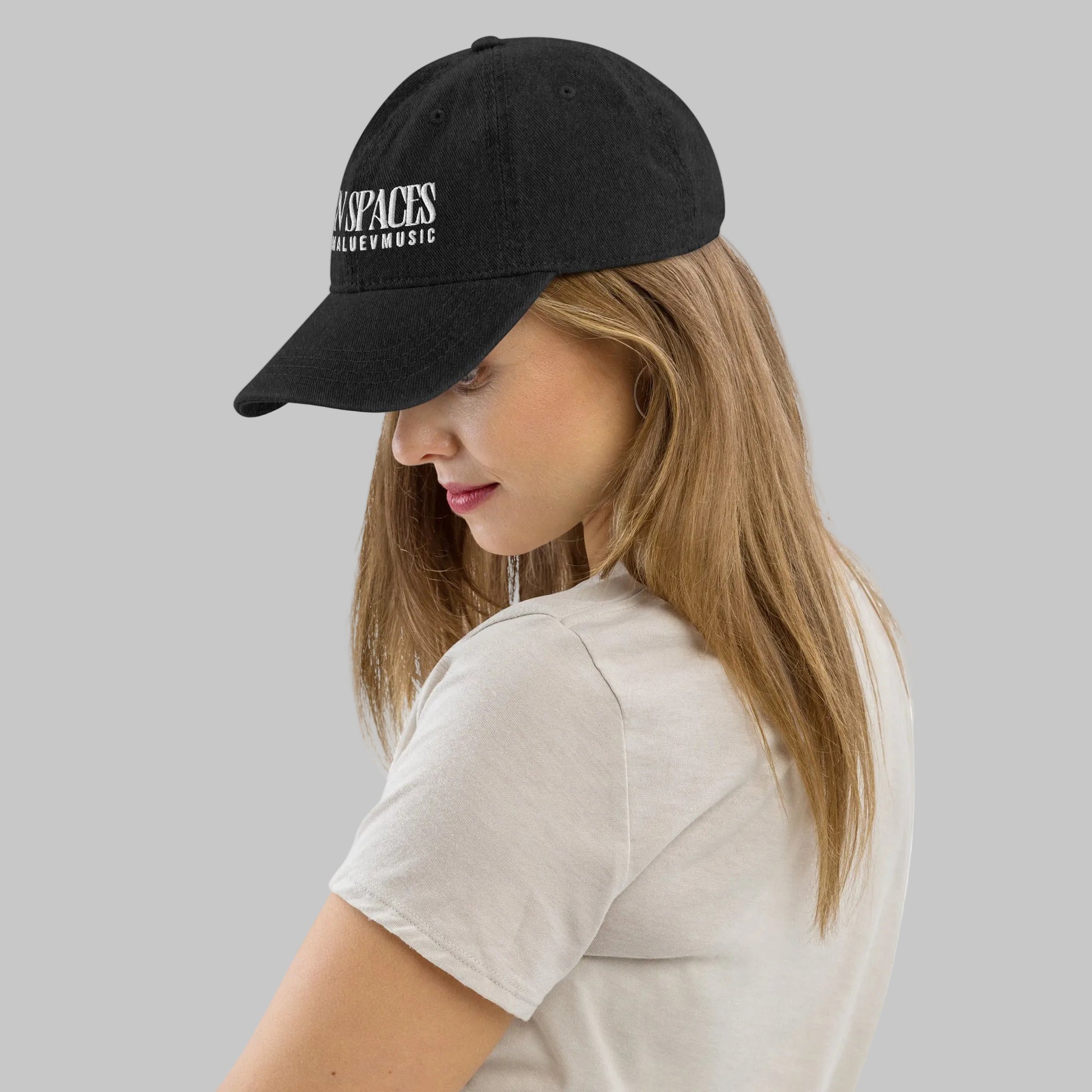 Woman wearing a black denim cap with text 'Open Spaces' and 'AShamaluevMusic' on a gray background.