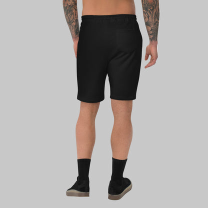 Man wearing black fleece shorts with embroidery 'MEGAPOLIS' and 'AShamaluevMusic' logo on the left leg and a drawstring waistband.