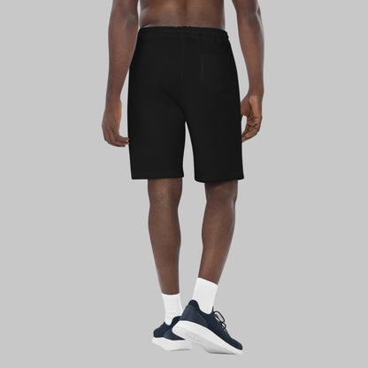 Man wearing black fleece shorts with embroidery 'MEGAPOLIS' and 'AShamaluevMusic' logo on the left leg and a drawstring waistband.