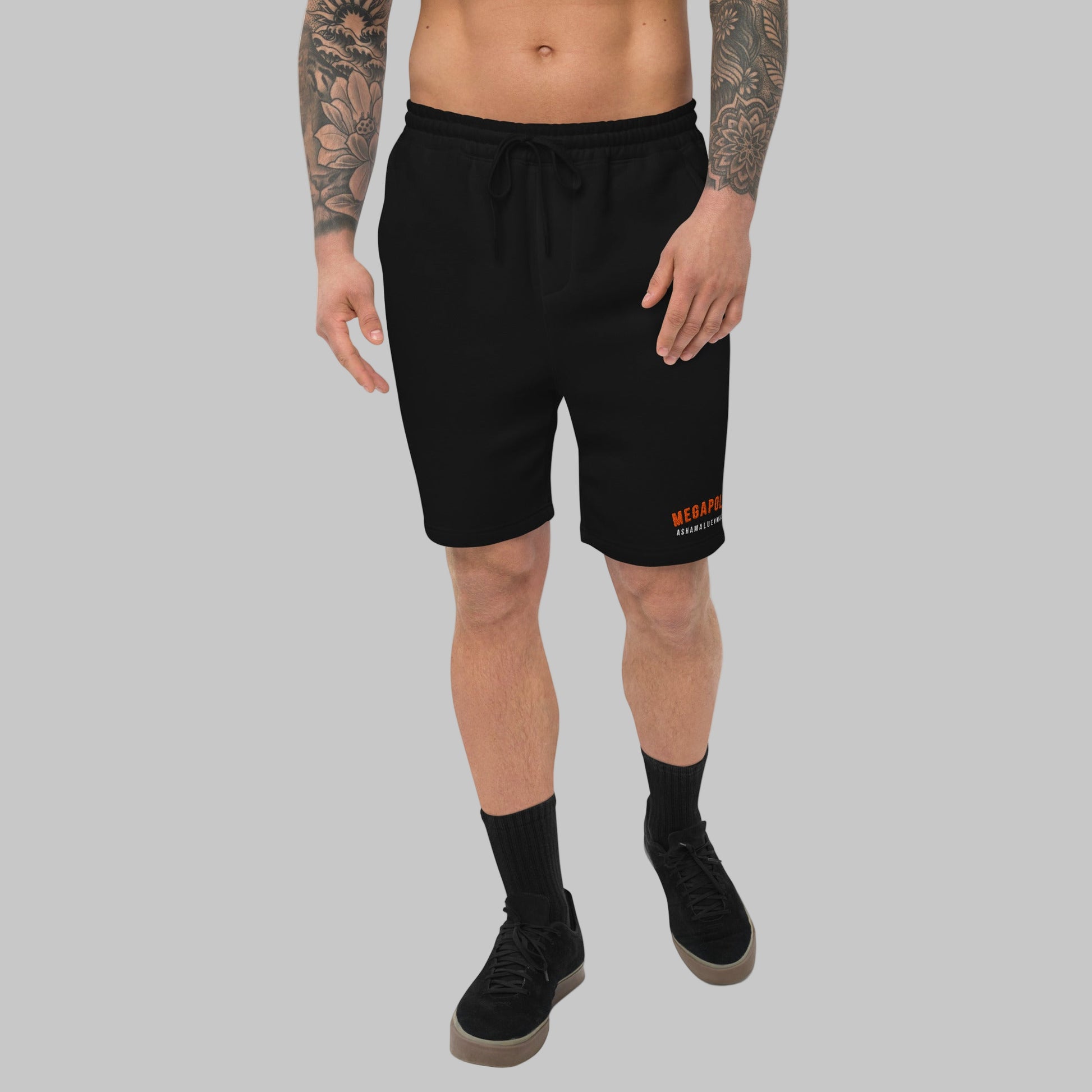 Man wearing black fleece shorts with embroidery 'MEGAPOLIS' and 'AShamaluevMusic' logo on the left leg and a drawstring waistband.