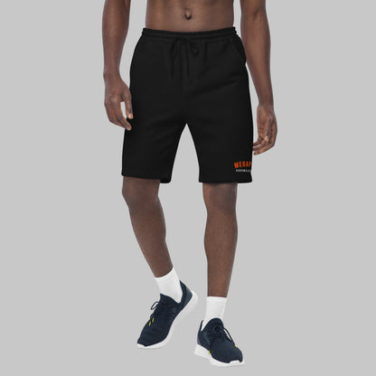 Man wearing black fleece shorts with embroidery 'MEGAPOLIS' and 'AShamaluevMusic' logo on the left leg and a drawstring waistband.