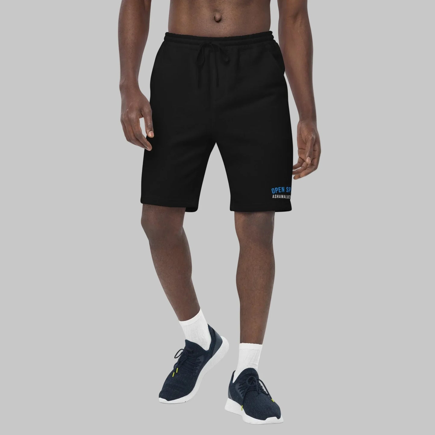Man wearing black fleece shorts with 'Open Spaces' and 'AShamaluevMusic' embroidered on a gray background