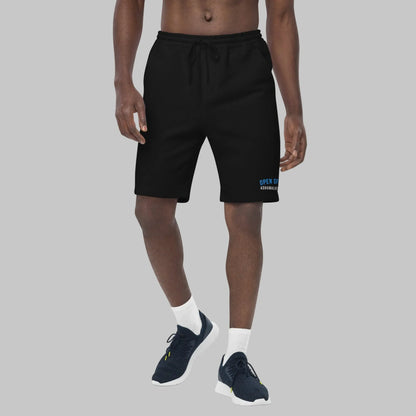 Man wearing black fleece shorts with 'Open Spaces' and 'AShamaluevMusic' embroidered on a gray background