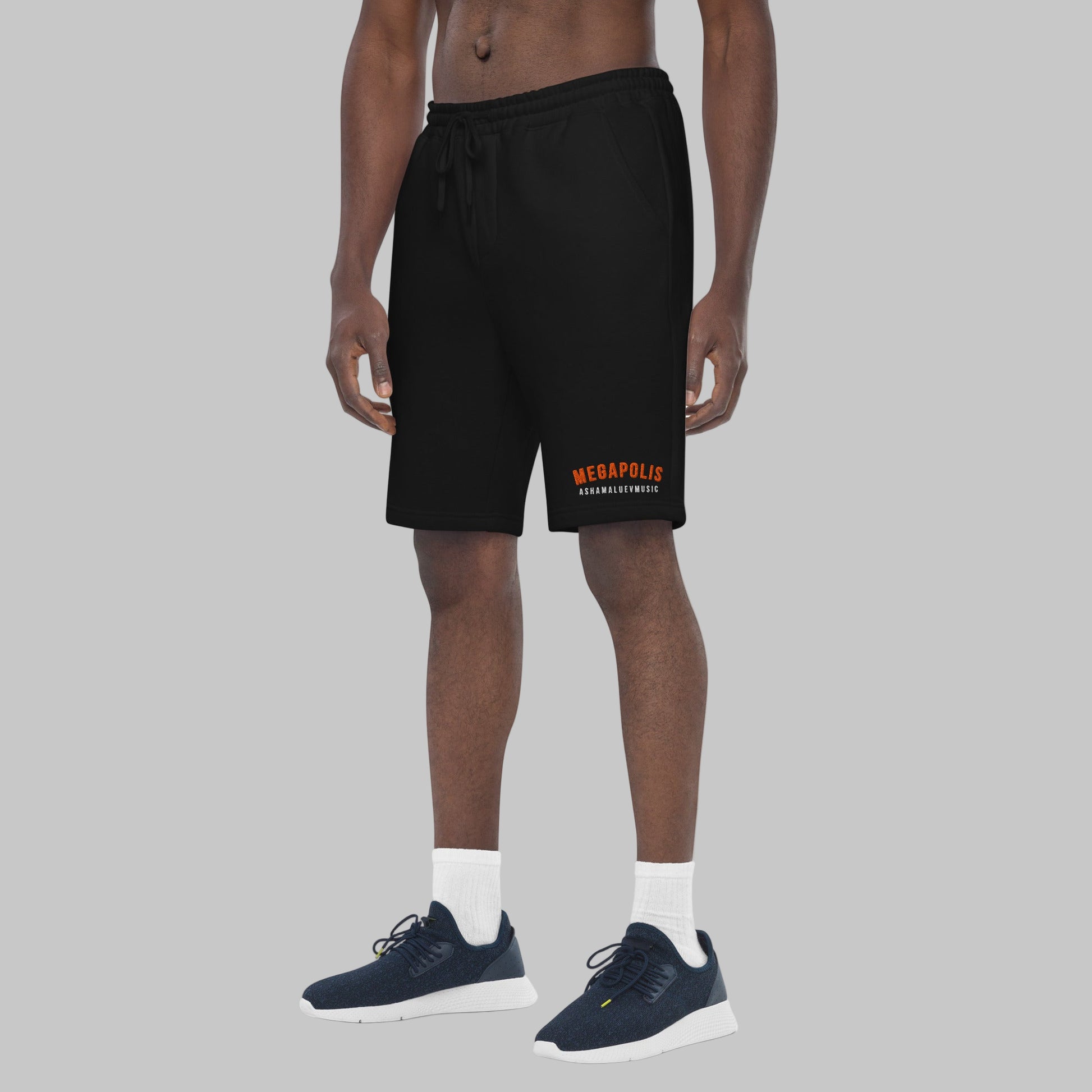 Man wearing black fleece shorts with embroidery 'MEGAPOLIS' and 'AShamaluevMusic' logo on the left leg and a drawstring waistband.