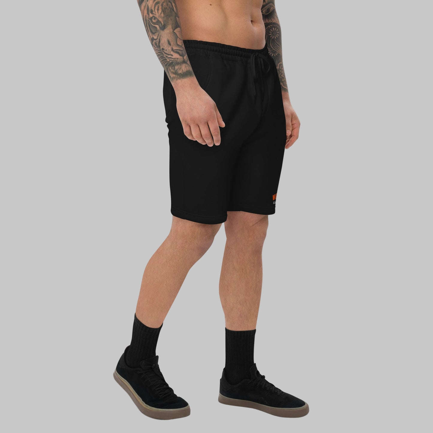 Man wearing black fleece shorts with embroidery 'MEGAPOLIS' and 'AShamaluevMusic' logo on the left leg and a drawstring waistband.