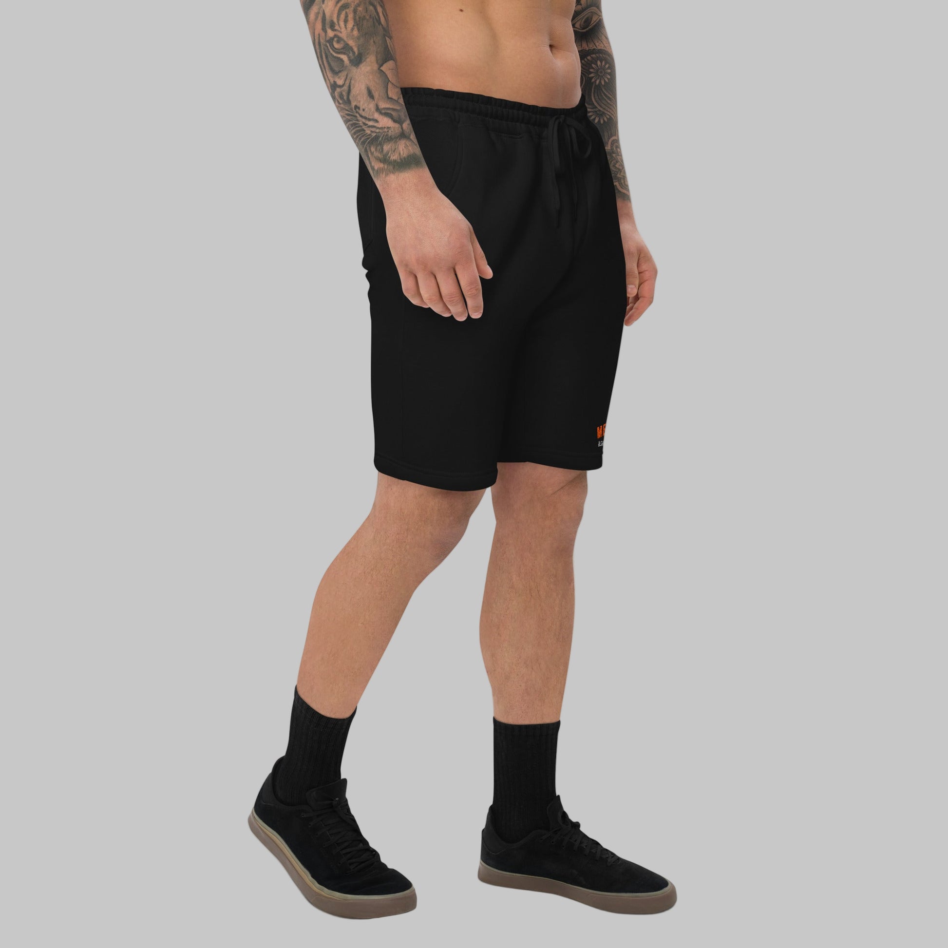 Man wearing black fleece shorts with embroidery 'MEGAPOLIS' and 'AShamaluevMusic' logo on the left leg and a drawstring waistband.