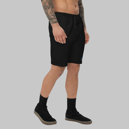Man wearing black fleece shorts with 'Open Spaces' and 'AShamaluevMusic' embroidered on a gray background