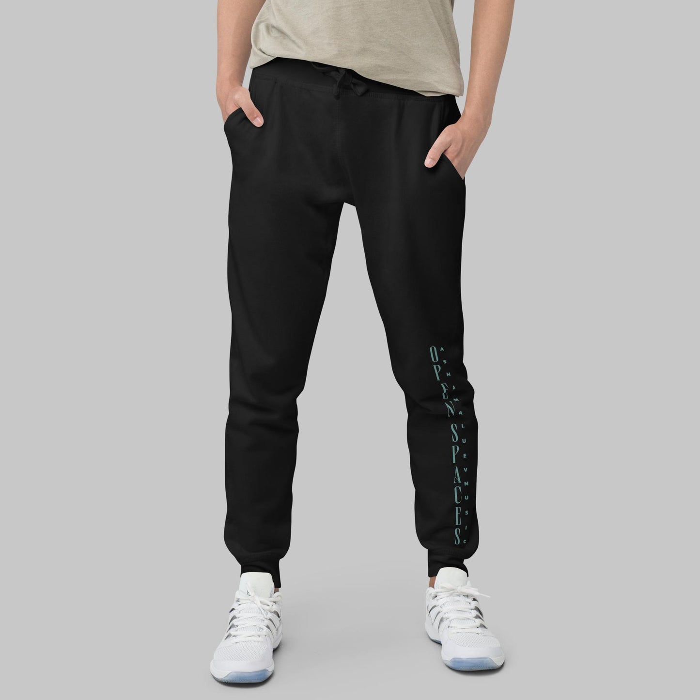 Man wearing black fleece sweatpants with text 'Open Spaces' and 'AShamaluevMusic' on the legs against a gray background