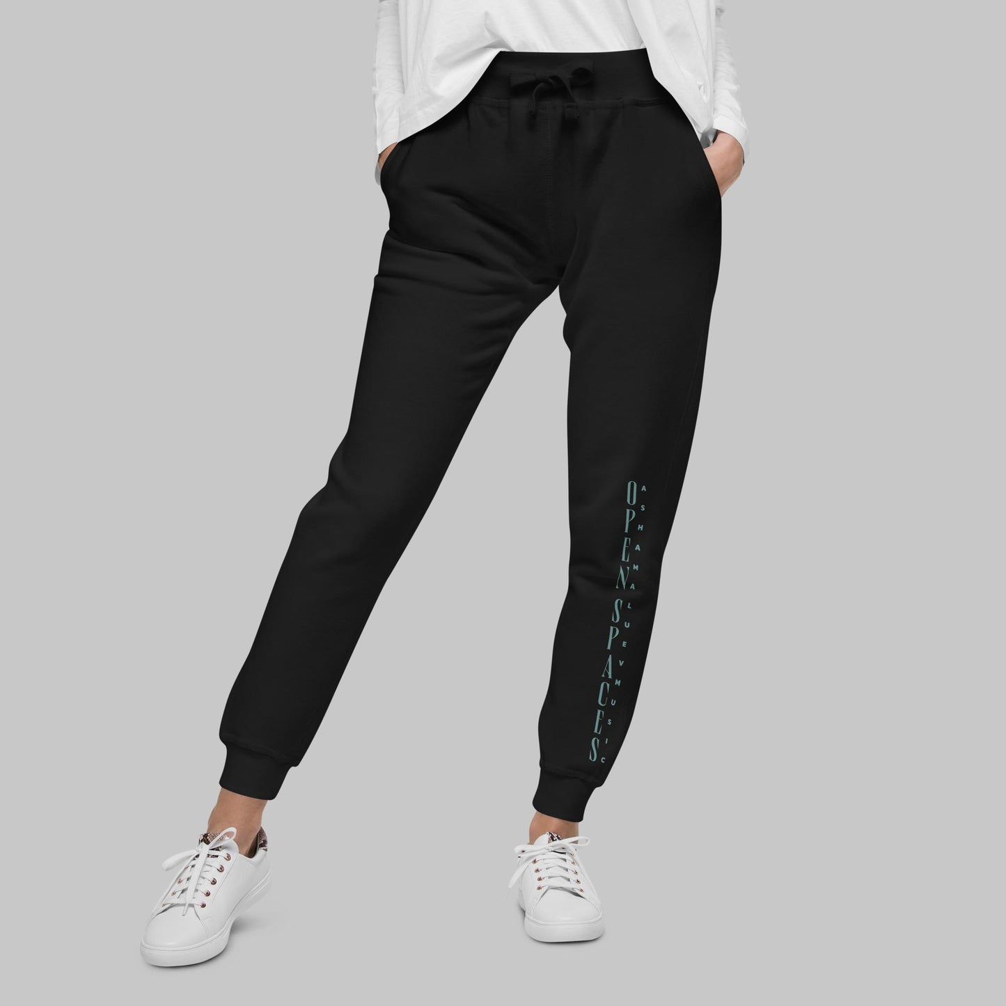 Woman wearing black fleece sweatpants with text 'Open Spaces' and 'AShamaluevMusic' on the legs against a gray background