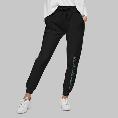 Woman wearing black fleece sweatpants with text 'Open Spaces' and 'AShamaluevMusic' on the legs against a gray background