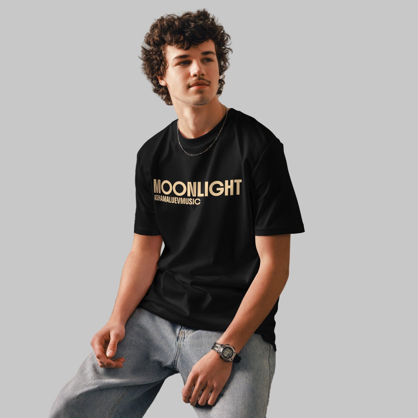 Man wearing a black organic cotton t-shirt with 'Moonlight' print and AShamaluevMusic logo on a light grey background