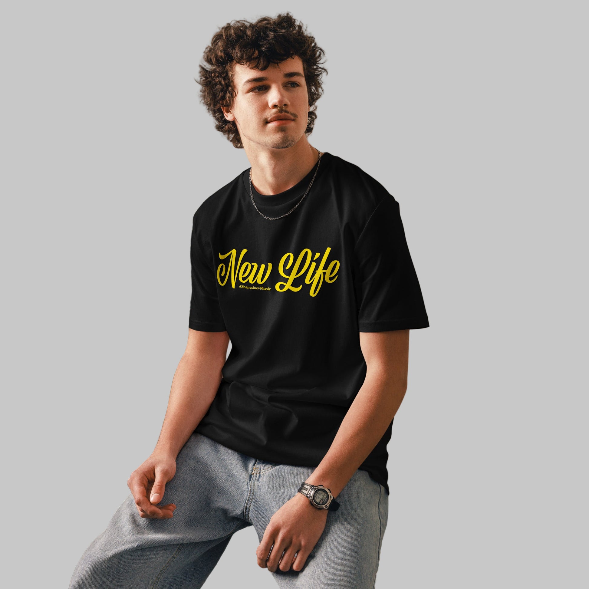 Man wearing a black organic cotton t-shirt with 'New Life' print and AShamaluevMusic logo in yellow text on a grey background