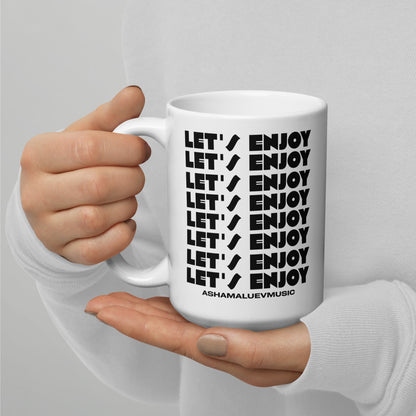 White mug with 'LET'S ENJOY' text held by a person against a gray background