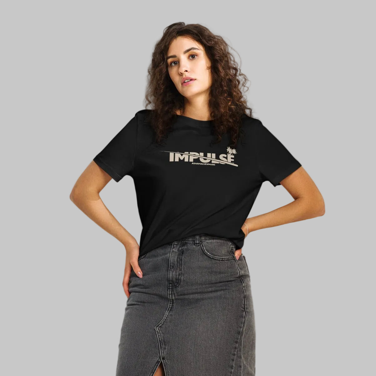 Woman wearing a black women's organic short sleeve t-shirt with beige text 'IMPULSE' and AShamaluevMusic on a gray background