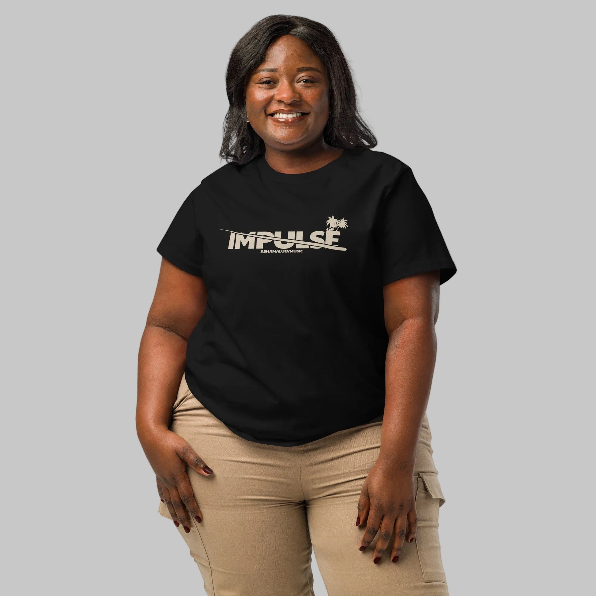 Woman wearing a black women's organic short sleeve t-shirt with beige text 'IMPULSE' and AShamaluevMusic on a gray background