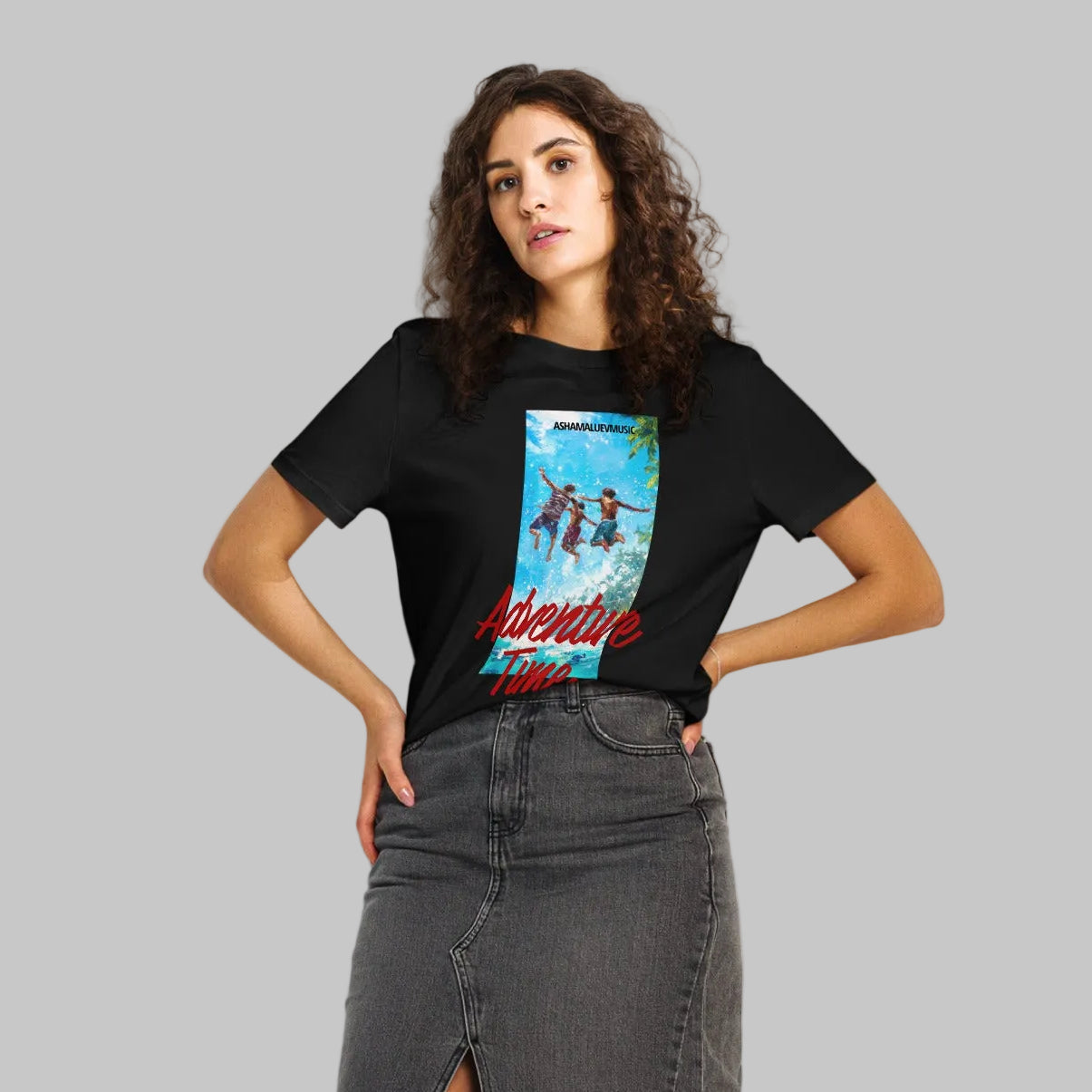 Woman wearing a black organic short sleeve t-shirt with a 'Adventure Time' colorful graphic and text 'AShanaluevMusic' on a gray background